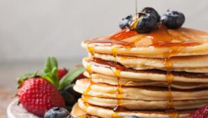 Pancakes topped with syrup, blueberries and strawberries served from the griddle combos breakfast menu at Wheaton Family Restaurant in Eau Claire, WI